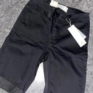 Svarta jeansshorts från Oiecee - Svarta jeansshorts från Oiecee med klassisk femficksdesign och uppvikta benslut. Modellen är midwaist och har en enkel, stilren look som passar till mycket. Perfekta för varma dagar när du vill ha något bekvämt och snyggt.