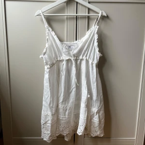 Vit sommarklänning från JDL - Fin sommarklänning från JDL som både passar till vardagen och till stranden. Klänningen är i kort längd, vit och lite genomskinlig.