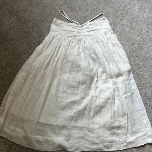 Vit långkjol  - Superfin vit långkjol från Jonathan Simkhai i luftig linneblandning. Kjolen har smala band som går över magen och dragkedja där bak