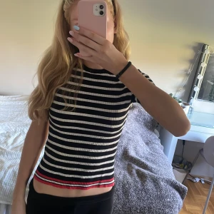 Randig ribbad topp från Zara - Säljer en svartvit randig ribbad topp från Zara med korta ärmar och rund hals. Toppen har en croppad passform och en röd detalj längst ner vid fållen som ger en snygg kontrast. Perfekt för dig som gillar en enkel men trendig stil.