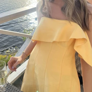 Balklänning från Aje - Säljer en solgul axelbandslös långklänning med volangdetalj upptill. Nypris är 7000kr. Klänningen har en elegant och luftig passform, perfekt för sommarens tillfällen. Tillverkad i ett lätt material som ger ett fint fall. Den har även fickor!