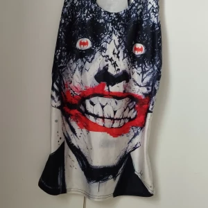 Brottarlinne med Joker-tryck - Unikt linne med stort tryck av Jokerns ansikte i svart, vitt och rött. Ögonen har Batman-loggan i rött och vitt, och det röda leendet är riktigt iögonfallande. Perfekt för dig som gillar serietidningar och vill sticka ut med din stil. 