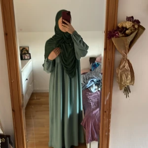 Lång grön klänning med puffärm från Turkiet! - Snygg långklänning i dämpad grön nyans med rund halsringning och puffiga långärmar med resår vid handlederna. Klänningen har en lös passform och faller fint ner till golvet. Perfekt för dig som gillar modest och stilren look.