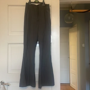 Grå kostymbyxor från Gina Tricot - Snygga grå kostymbyxor från Gina Tricot med klassisk passform och utsvängda ben. Byxorna har hög midja och stängs med dragkedja framtill. Perfekta för en stilren look.