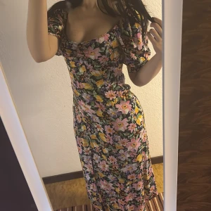 Blommig långklänning med puffärm - Supersöt långklänning med färgglatt blommönster i rosa, gul, lila och grönt. Klänningen har offshoulder-modell med puffiga korta ärmar och smickrande passform. Perfekt för sommarens alla tillfällen!