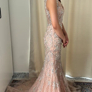 Glittrig långklänning med pärlor och paljetter - Säljer en lyxig långklänning i ljus champagnefärg, täckt av pärlor och paljetter. Klänningen har v-ringning, är ärmlös och figurnära passform. Perfekt för bal eller fest. Materialet känns exklusivt och skimrar vackert i ljuset.