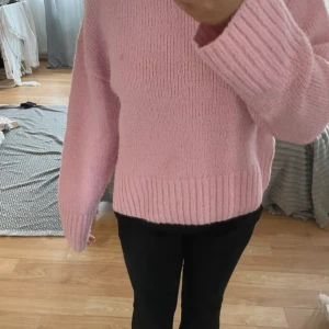 Ljusrosa stickad tröja - Mysig ljusrosa stickad tröja med lång ärm och bred ribbad kant nedtill och vid ärmslut. Perfekt för kyligare dagar och enkel att matcha med olika outfits.