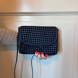 Lik Bottega Veneta mörkblå flätad axelväska - Säljer en mörkblå axelväska med flätad design och lång axelrem. Den stängs med en knapp. Kan bäras som clutch eller axelremsväska.