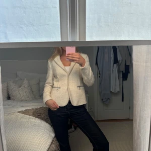 Vit kavaj med dragkedjedetaljer - Snygg vit kavaj med dragkedjedetaljer vid fickorna. Klassisk krage och figurnära passform, perfekt till jeans eller kjol. Stängs med en knapp framtill. Stilren och enkel att matcha.