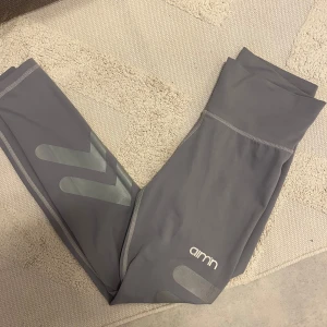 Grå träningstights från aim'n - Snygga grå tights från aim'n med hög midja och diskreta reflexdetaljer på benen. Perfekta för gymmet eller löprundan. Mjukt och stretchigt material som sitter skönt på kroppen.