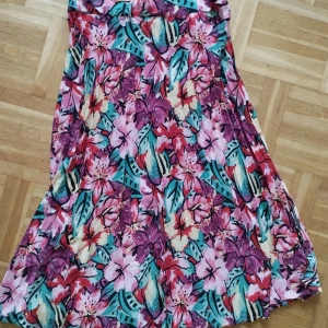 Blommig kjol från Springfield - Färgglad lång kjol från Springfield med blommigt mönster i rosa, rött, grönt och lila. Kjolen har slits och en luftig passform, perfekt för varma dagar. Tillverkad i 100% polyester.
