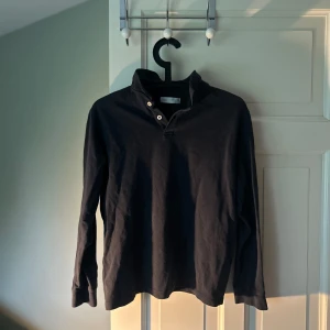 Svart långärmad pikétröja från Zara - Säljer en svart långärmad pikétröja från Zara i storlek 164 (13-14 år). Tröjan har klassisk krage med knappar och är tillverkad i mjuk bomull. Perfekt för en stilren och enkel look.