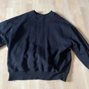 Svart sweatshirt från Sweet Sktsb - Säljer en svart sweatshirt från Sweet Sktsb med stor vit logga broderad på ryggen. Tröjan har rund halsringning, långa ärmar och breda ribbade muddar vid ärmslut och nederkant. Perfekt för en avslappnad streetstil.