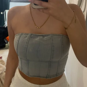 Ljusblå croppad tubtopp i jeansmaterial - Säljer en ljusblå croppad tubtopp i jeansmaterial med markerade sömmar och dragkedja i ryggen. Perfekt för dig som vill ha en trendig och stilren topp till sommaren.