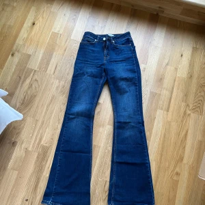 Mörkblå bootcut jeans från NAKD - Säljer ett par mörkblå bootcut jeans från NAKD kollektion med Kae Sutherland. klassisk femficksdesign och medel hög midja. Jeansen har dragkedja och knapp framtill samt snygga kontrastsömmar. Lite slitna nedtill i benen bak pga långa och jag är 160 lång.