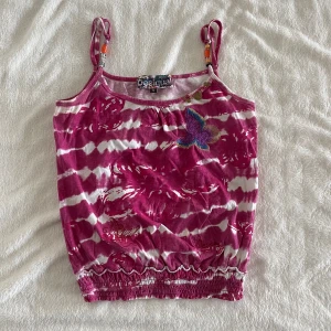 Rosa och vit batikmönstrad linnetopp från Desigual - Säljer en färgglad rosa och vit batikmönstrad linnetopp från Desigual med broderade fjärilar och pärldetaljer på axelbanden. Toppen har smockad nederkant och tunna axelband med pärlor. Perfekt för sommardagar!