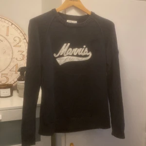Mörkblå stickad tröja från Morris - Snygg mörkblå stickad tröja från Morris med broderad logga framtill och patch med brittisk flagga på ärmen. Klassisk rund halsringning och långa ärmar. Perfekt för dig som gillar stilrena plagg med detaljer.