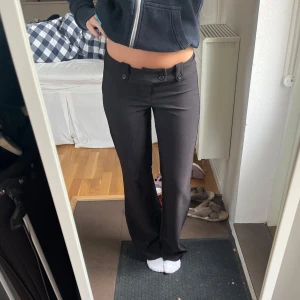 Svarta kostymbyxor  - Snygga svarta kostymbyxor med två dekorativa knappar i midjan och raka ben. Byxorna har normal passform och klassisk look, perfekta för en stilren outfit.