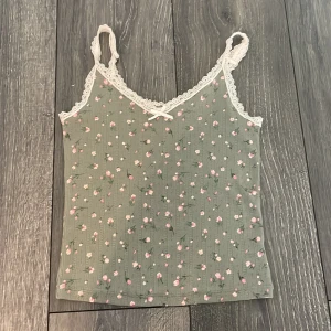 Grön blommig linnetopp med spets från H&M Divided - Supersöt grön linnetopp med små rosa och vita blommor, spetskant runt halsringningen och axelbanden samt en liten rosett framtill. Perfekt för varma dagar eller som ett lager under en kofta.