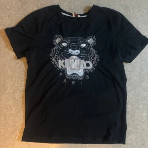 Svart t-shirt med broderad tiger från Kenzo - Säljer en svart t-shirt från Kenzo med stort broderat tigerhuvud och logga på bröstet. T-shirten har rund hals och korta ärmar. Perfekt för dig som gillar statement-plagg och streetwear.