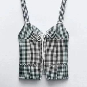 Rutig croppad linnetopp med knyt - Supersöt croppad linnetopp med svartvitt rutigt mönster och breda axelband. Toppen har knyt framtill och en figurnära passform. Perfekt för sommardagar och att styla med jeans eller kjol.