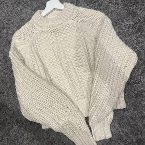Beige stickad tröja från H&M - Säljer en chunky beige stickad tröja från H&M med grovstickat mönster och rund hals. Perfekt för lager-på-lager och passar till allt. Tröjan har långa ärmar och breda muddar vid ärmslut och nederkant. Den är även lite cropped. 