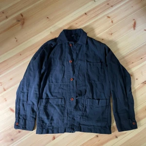 Mörkblå overshirt med röda knappar - Säljer en mörkblå overshirt med tre stora fickor framtill och röda knappar. Jackan har klassisk krage och lång ärm, perfekt för lager-på-lager. Enkel och stilren design som funkar till mycket. Köpt i arbetarboden i stockholm nästan helt oanvänd. Väldigt fin jacka som är tillverkad i italien av ett litet lokalt företag som gör allt förhand och tar beställningar. Org pris 2000. Skriv för frågor :)