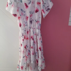 Blommig vit klänning med volang - Säljer en söt vit klänning med blommigt mönster i rosa och lila toner. Klänningen har korta ärmar, resår i midjan och volang nertill. Perfekt för sommarens alla tillfällen!