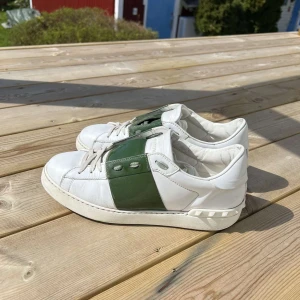Valentino Open sneakers i vitt och grönt - Säljer ett par snygga Valentino Open sneakers i vitt skinn med grönt band över mitten. Klassisk rund tå, vita snören och platt sula. Perfekta för dig som gillar stilrena och exklusiva sneakers.