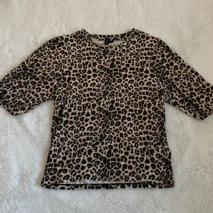 Leopardmönstrad topp från lager 157 - Säljer en snygg leopardmönstrad topp från The Black Label Collection (lager 157). Toppen har korta ärmar och är i mjukt material, perfekt för att sticka ut lite extra. Färgerna är beige och svart.