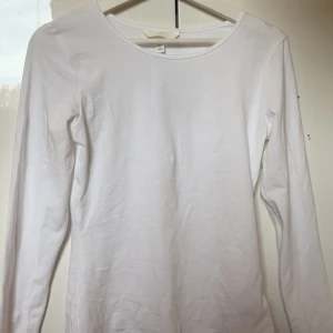 Vit långärmad topp - En enkel och stilren vit långärmad topp med rund halsringning. Perfekt basplagg som passar till det mesta. Mjuk och skön bomullskvalitet. Prislapp sitter kvar