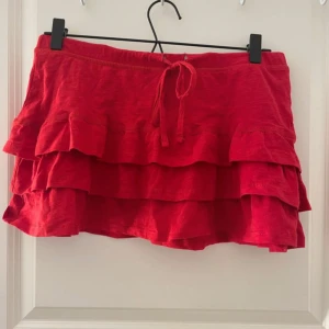 Röd volangkjol med knytband - Superfin röd kortkjol med flera volanger och knytband i midjan. Perfekt för dig som vill ha en färgstark och lekfull look. Kjolen har en mjuk och bekväm passform och är lätt att matcha med olika toppar.