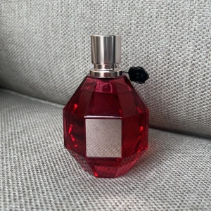 Flowerbomb Ruby Orchid Eau de Parfum - En lyxig parfym från Viktor & Rolf, Flowerbomb Ruby Orchid, i en röd, multifasetterad glasflaska med silverfärgat sprayhuvud och metallisk etikett. Flaskan har en unik diamantform och en svart dekordetalj vid halsen. Testad 