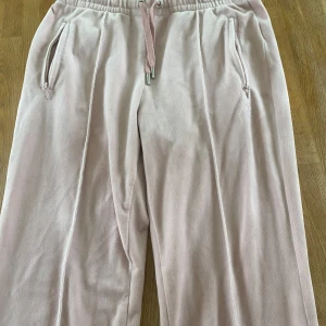 Ljusrosa mjukisbyxor från Juicy Couture - Säljer ett par ljusrosa mjukisbyxor från Juicy Couture med dragsko i midjan och fickor med dragkedja. Baktill står det 'Juicy' i glittriga stenar. Perfekta för en avslappnad och trendig look. Köparen står för frakt!