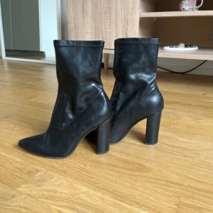 Svarta boots med klack och spetsig tå - Säljer ett par svarta boots med hög klack och spetsig tå. Skorna har en stilren design och är perfekta för att lyfta vilken outfit som helst. De har en rundad skaftkant och en stadig blockklack.