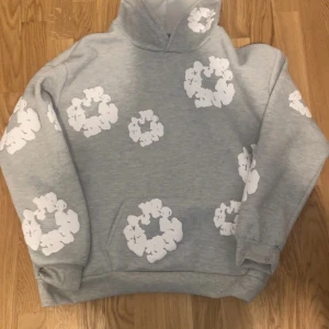 Grå hoodie från Denim Tears - Säljer en grå hoodie från Denim Tears med ett unikt vitt blommönster. Storlek S men passar M är stor i storleken. Aldrig använd för den var för stor på mig. Skriv för fler frågor 
