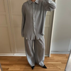 Gråblå set - Säljer detta ribbade setet i en gråblå färg. Setet är i stretchigt material och ganska oversized i modellen. Passar till någon som brukar ha XS/M. Byxorna är långa, så de funkar jättebra med klackar, men går också att vika upp i midjan om man vill ha dem kortare. Tyget är mjukt och skönt. Det går bra att steama plaggen för att behålla den ribbade strukturen.   Setet är knappt använt och i väldigt fint skick. Säljes endast tillsammans.   Skjorta: stl 36 Byxor: stl 34  Material: 100 % polyester