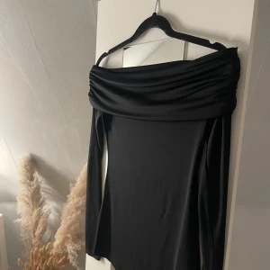 Svart offshoulder topp från H&M MAMA - Säljer en svart långärmad offshoulder topp från H&M MAMA i stretchigt material. Toppen har en bred, draperad krage som ger en snygg och modern look. Perfekt för dig som vill ha något stilrent och bekvämt. Aldrig använts.