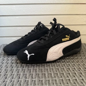 Puma Speedcats  - Säljer ett par svarta Puma sneakers med vit sidosula och vit Puma-logga framtill. Skorna har snörning och är tillverkade i mocka med klassisk design och guldfärgad Puma-text på sidan.