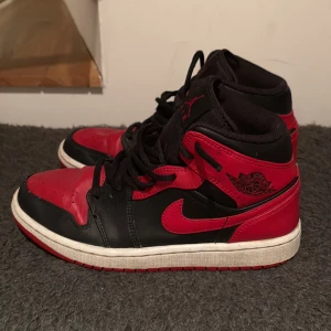 Nike Air Jordan 1 Retro mid OG Bred 40,5 - Säljer ett par klassiska Nike Air Jordan 1 Retro High OG i svart och rött med vita sulor. Skorna har snörning, rund tå och är tillverkade i skinn. Perfekta för dig som gillar ikoniska sneakers med streetkänsla. Skorna är i strl 40,5 (UK 6,5). Självklart äkta. Skorna ingår endast. De är bara att höra av dig vid närmaste fundering🙌😀