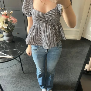 Svartvit rutig blus med puffärmar - Supersöt blus i svartvitt rutigt mönster med puffiga korta ärmar och v-ringning. Modellen är lite lösare nertill och har en volangkant som ger en romantisk känsla. Perfekt att styla med jeans eller kjol.