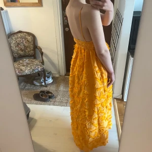 Orange långklänning med struktur och smala axelband - Säljer en organge långklänning med smala axelband och djup rygg. Klänningen har en markerad midja med resår och är täckt av dekorativa, strukturerade detaljer som ger en unik look. Perfekt för sommarens alla tillfällen.