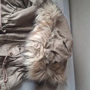 Beige parkajacka med fuskpäls - Snygg beige parkajacka från H&M med mysigt teddyfoder och huva med fuskpäls. Jackan har dragsko i midjan, stora fickor framtill och stängs med dragkedja och knappar. Perfekt för kyliga dagar. Jag köpte den för 465 kr. Gör dig varm inom några minuter värd att köpa om den igen. Me. Jag har blivit längre  jag är 177 cm 