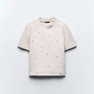 Vit kortärmad tröja med pärlor från Zara - Säljer en stilren vit tröja från Zara med korta ärmar och rund halsringning. Tröjan är dekorerad med små pärlor framtill för en extra detalj. Perfekt för dig som vill ha något enkelt men ändå speciellt.