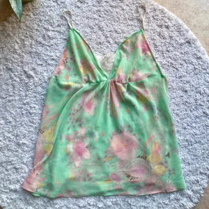 Mintgrön topp - Mintgrön topp med blommor, små bin och spetsdetaljer. Smala justerbara axelband. Tunt material, sannolikt polyester. Har en liten lagning som syns på bild 4, inget som syns när man har den på sig. Ingen lapp, men ett bildsök visar att det är äldre vintage H&M design. Passar S och M.