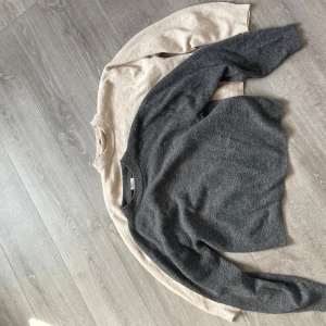Två stickade tröjor i grått och beige - Säljer två mysiga stickade tröjor, en i mörkgrå och en i ljusbeige. Båda har rund halsringning, perfekta för lite varmare sommarkvällar