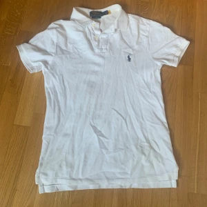Vit piké t-shirt från Polo Ralph Lauren - Vit piké t-shirt från Polo Ralph Lauren med klassisk krage och knappar framtill. Slim fit-modell med korta ärmar och broderad logga på bröstet. Perfekt för sommaren. Nypris c:a 1200 kr. Använd fåtal gånger. Inga synliga defekter. Storlek small