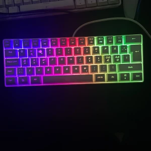 Mekaniskt tangentbord MX5 med RGB-belysning - Säljer ett kompakt mekaniskt tangentbord från MX5 med snygg RGB-belysning som lyser i flera färger. Tangentbordet har nordisk layout med specialtecken som Æ och Ø. Perfekt för gaming eller skrivarbete. Ansluts med kabel och har vit botten. Priset kan diskuteras.