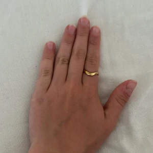 Guldring - Säljer en stilren guldfärgad ring med vågig design. Ringen är öppen baktill vilket gör den justerbar i storlek. Perfekt för dig som gillar minimalistiska smycken med en twist. Ringen är från olympia rings