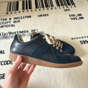Maison Margiela skor - Säljer ett par blå Maison Margiela sneakers med beige snörning och gummisula. Skorna har en mix av mocka och skinn, klassisk design och rund tå. Perfekta för dig som gillar stilrena och tidlösa sneakers. Skick 10/10👏👏👏